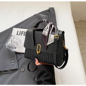 Detail of black leather handbag with woven texture and decorative silk scarf on handle