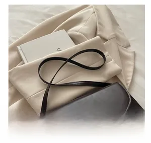 Detail view of a vintage dark brown shoulder bag on a beige blazer with artsy book background