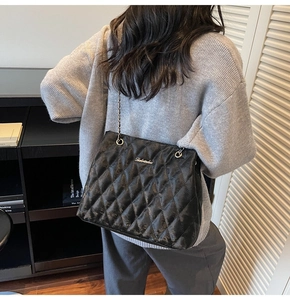 Close-up of black quilted leather shoulder bag with gold chain and metal logo detail