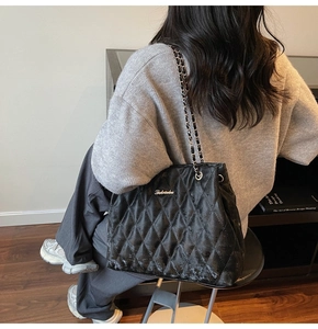 Detail of black quilted tote bag with silver chain strap and metal logo on a model
