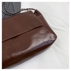 Détail du sac à bandoulière en cuir verni marron foncé avec chaîne et texture brillante