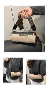 Detail view of beige suede cylinder bag with black leather trim and wide patterned strap