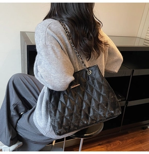 Quilted black tote bag detail with leather chain strap and gold logo on model