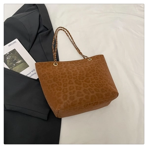 Détail du sac cabas léopard avec bandoulière chaîne dorée sur fond en tissu blanc élégant