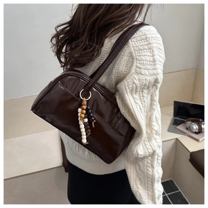 Detail of dark brown patent leather tote bag with stylish beaded charm and gold hardware