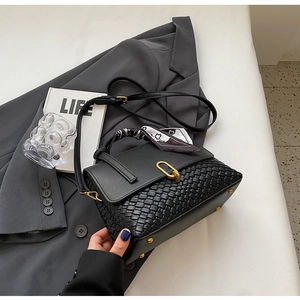 Detail of black woven handbag with silk scarf handle and gold lock on a grey suit
