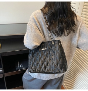 Detail of black quilted tote bag with chain strap and metal logo on smooth leather