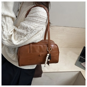 Detail of a brown leather shoulder bag with beaded pendant worn over a white sweater
