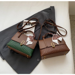 Detail of woven flap handbag with metal clasp and printed silk scarf accessory