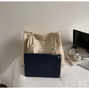 Detail showing spacious beige tote bag capacity with laptop and accessories on bed