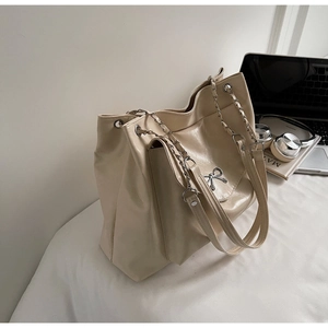 Chic beige tote bag with metal bow detail and chain strap shown in a lifestyle setting