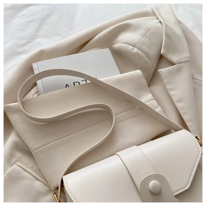 Gros plan sur un sac bandoulière beige minimaliste avec boucle ronde sur un blazer