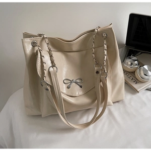 Detail of beige tote bag with silver bow accent and metal chain handle on office desk