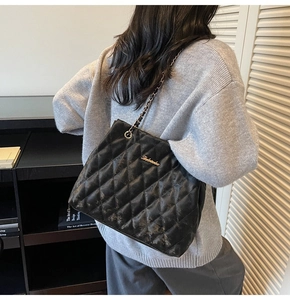 Detail of black quilted leather tote bag with metal chain strap and golden logo
