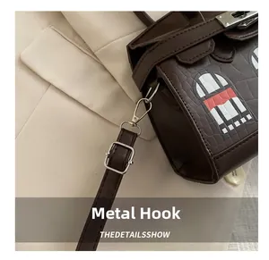 Detail of silver hardware hooks and adjustable leather strap on a brown embossed handbag