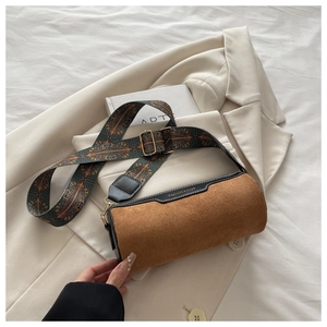 Detail of cylinder crossbody bag featuring brown suede texture and vintage jacquard strap