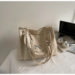 Close-up of cream tote bag with elegant metal bow detail and hybrid chain strap