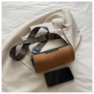 Detail view of mini cylinder bag in brown suede with ethnic print strap and phone for scale