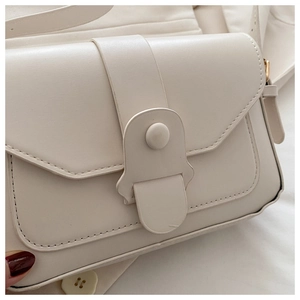 Gros plan du sac bandoulière beige en similicuir avec surpiqûres et boucle métallique
