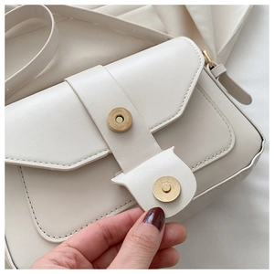 Détail du sac en cuir crème montrant les coutures fines et le fermoir magnétique doré