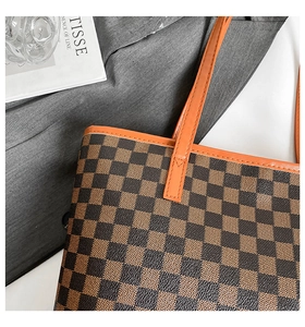 Close-up of checkered pattern tote bag with orange leather handles and detailed stitching