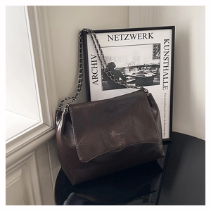 Sac bandoulière en cuir froissé marron foncé avec bandoulière chaîne sur surface miroir
