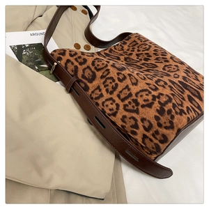 Close-up of leopard print tote bag with adjustable brown leather strap on a beige trench coat
