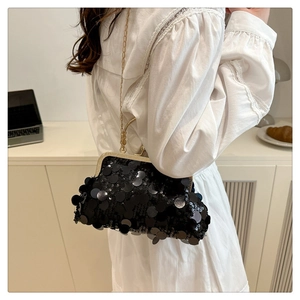 Chic black sequin shell bag with gold chain strap worn by a woman in a lace dress