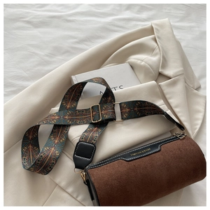 Detail view of brown suede cylinder bag featuring a colorful woven strap and gold hardware