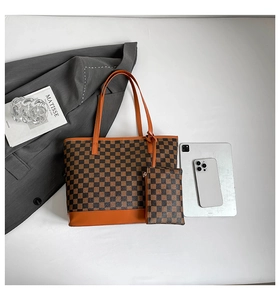 Flat lay of brown checkered tote bag with orange straps next to a tablet and art book