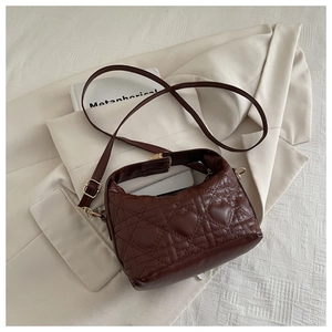 Detailed view of chocolate brown heart-quilted leather handbag on a beige textured background