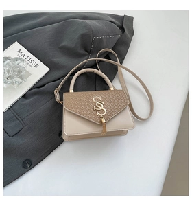 Detail of a beige handbag with woven brown flap, golden S-logo and fringe tassel detail
