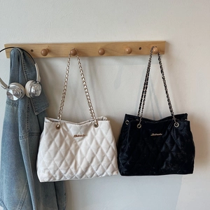 Chic quilted tote bags in beige and black velvet with metallic chain straps on wooden rack