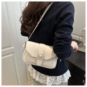 Detail of a creamy leather square shoulder bag featuring a cylindrical buckle and stitching