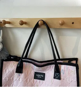 Pink quilted tote bag with colorful embroidery and black straps in a lifestyle setting