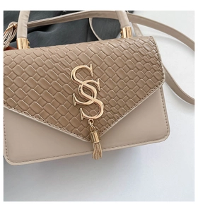 Detail of beige shoulder bag featuring woven texture flap and golden tassel hardware