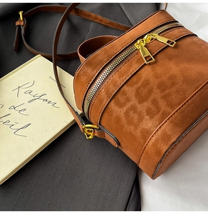 Detail der karamellbraunen Wildleder-Beuteltasche mit Gold-Reißverschlüssen und Riemen