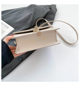 Detail view of a beige structured flap bag featuring a delicate gold tassel charm and strap