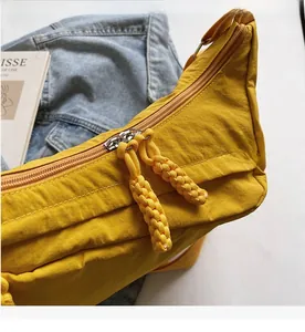 Detail of silver metal zipper with yellow woven pullers on a nylon crossbody bag