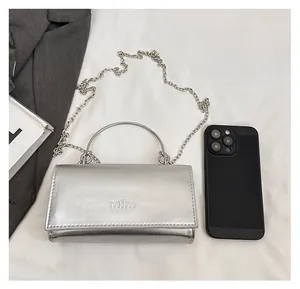 Silver leather mini bag with chain strap and round handle showing size comparison