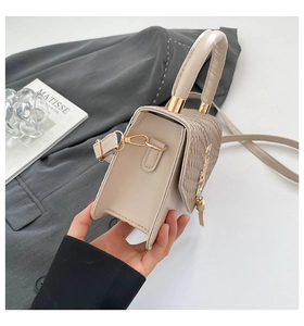 Side profile of a cream woven shoulder bag with gold logo and tassel detailing