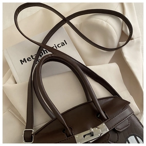 Detail of dark brown croc-embossed handbag featuring a silver twist lock and slim shoulder strap