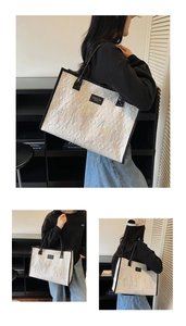 Detail of white quilted tote bag with colorful embroidery and black contrast handles