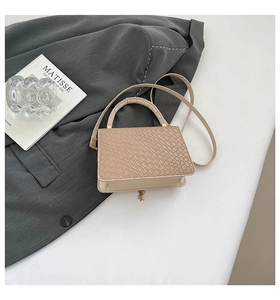 Detailed view of beige woven texture handbag with gold pendant on a charcoal suit background