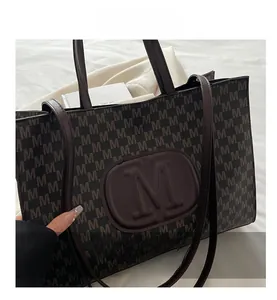 Detail of dark brown tote bag featuring embossed M logo and all-over letter print