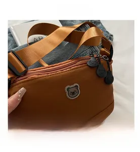 Detail view of caramel crossbody bag featuring double zippers and cute bear badge accent