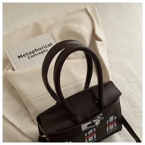 Detail of dark brown leather handbag with house-pattern appliqué and metal clasp
