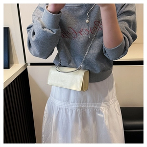Detail view of cream mini shoulder bag with chain strap on model with grey hoodie