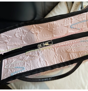Macro shot of the black zipper closure and wave embroidery on a pink quilted tote bag