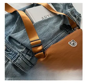 Close-up of brown nylon crossbody bag with bright orange adjustable strap and bear logo